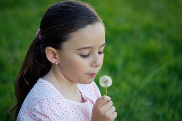 A pretty girl blowing dandelion in the grass