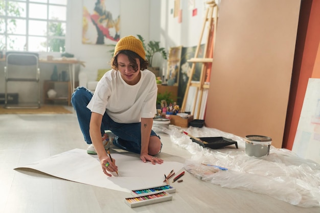 Photo pretty girl in casualwear sitting on the floor and drawing on paper