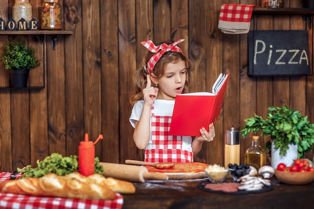 Pretty girl in checkered apron reading recipes book