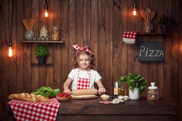 Pretty girl in checkered apron rolling out dough for pizza