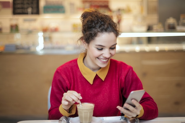 Photo pretty girl checking her smartphone in a café