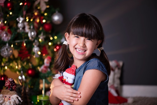 Pretty girl in Christmas decoration hugging a Santa Claus doll