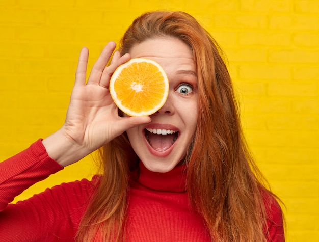 Pretty girl covering eye with an orange slice