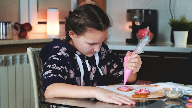 Pretty girl decorating cookies with color sugar glaze in the evening at home