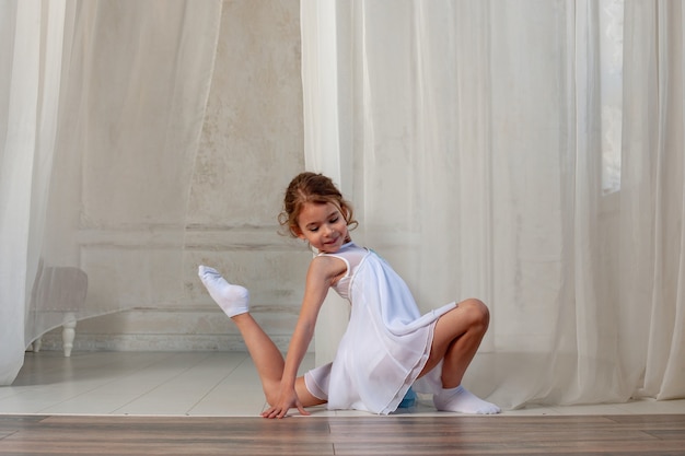 pretty girl does gymnastics in a dress on the background of a white curtain