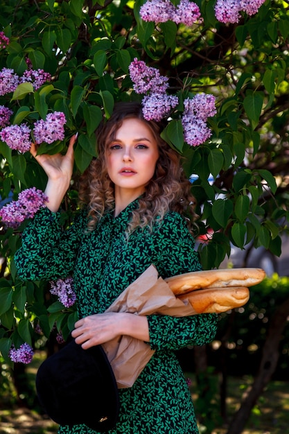 Pretty girl dressed in French style with baguette in hand and in lilac. French style Paris. Close-up French woman in stylish clothes holding fresh baguettes and smiling. Place for inscription or logo