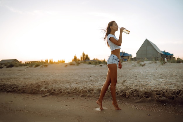 Pretty girl drinking beer while having party at the beach at sunset woman enjoying on beach holiday