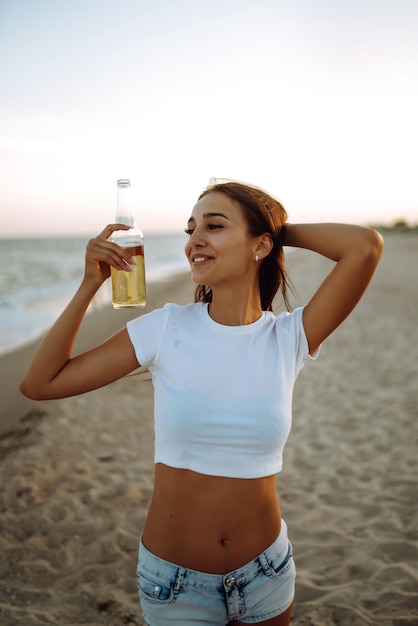 Pretty girl drinking beer while having party beach at sunset Young woman enjoying on beach holiday