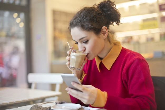 Bella ragazza bere caffè e controllando il suo smartphone