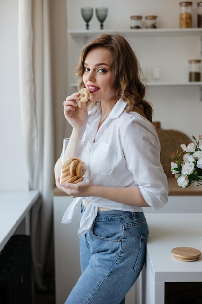 Красивая девушка ест печенье на кухне.