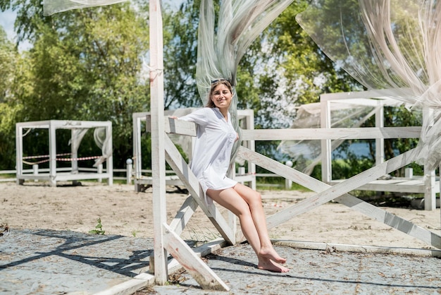 Photo pretty girl enjoy nature at sunny day in white wooden gazebo near the lake. freedom