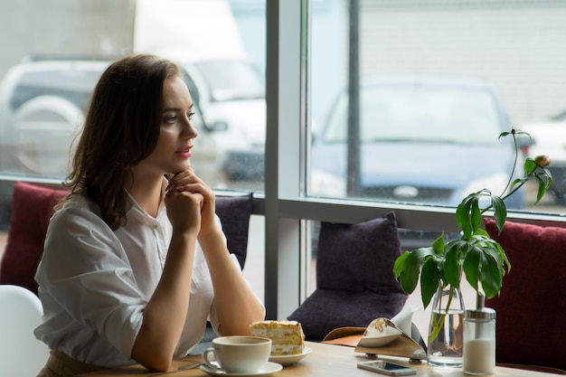 Pretty girl enjoys a fragrant coffee and sweet cake sitting in coffee house. Business woman resting during break.