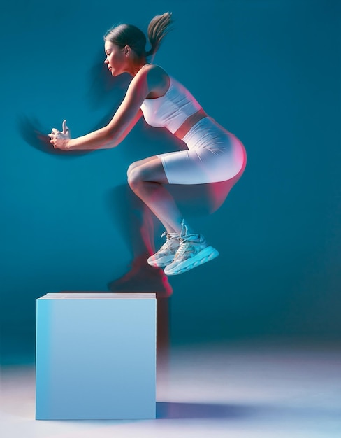 かわいい女の子が青い背景に白いスポーツユニフォームを着て白い立方体に飛び乗る、のコンセプト