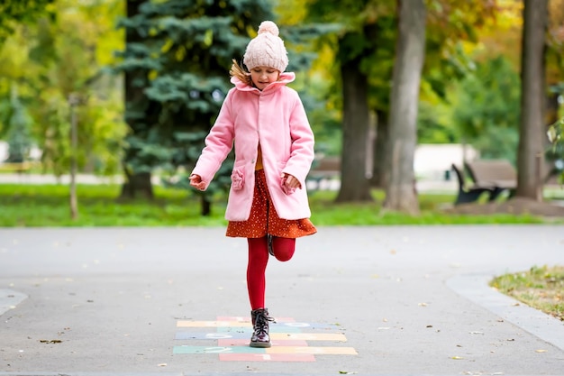 かわいい女の子の子供の通りでジャンプし、放課後に秋の日の幸せな子供の肖像画の屋外で遊んで