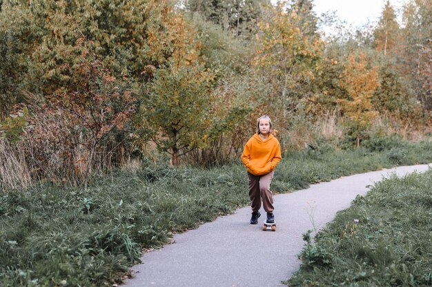 Bella ragazza che impara a fare skateboard all'aperto in una bella giornata autunnale. attività per bambini e concetto di stile di vita attivo.