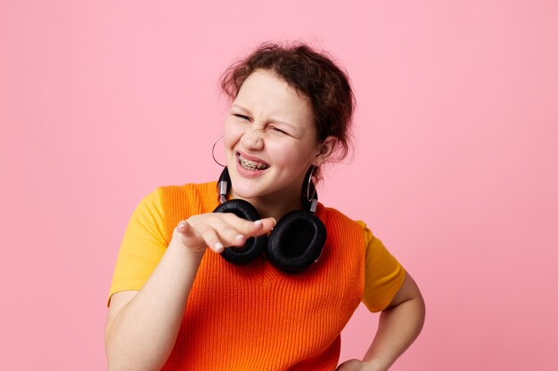 Pretty girl listening to music with headphones orange sweater emotions fun cropped view unaltered