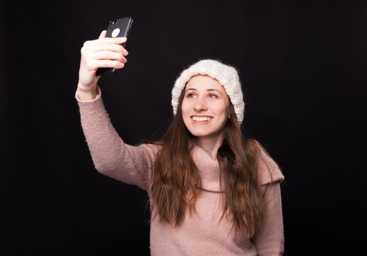 Фотография красивая девушка делает селфи со своим телефоном на черном фоне.