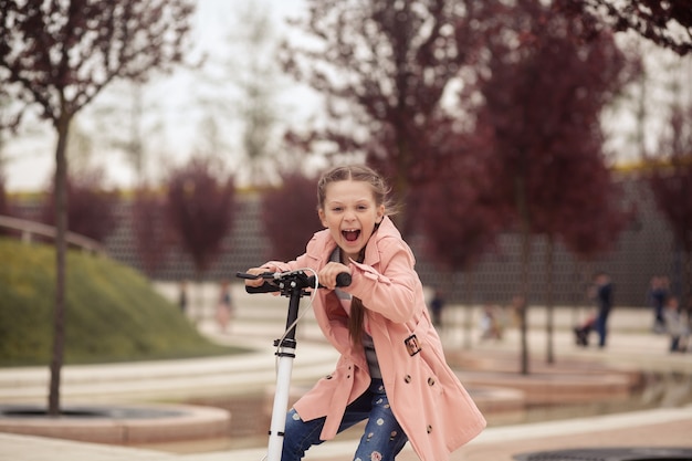 pretty girl in a pink raincoat riding in a scooter in park