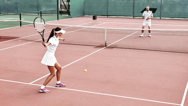 Bella ragazza gioca a tennis sul campo all'aperto si prepara a battere su una palla