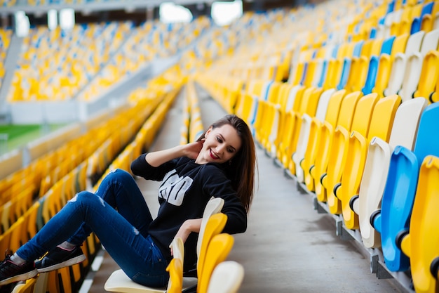 Красивая девушка сидит на школьном стадионе. Отдых от учебы.