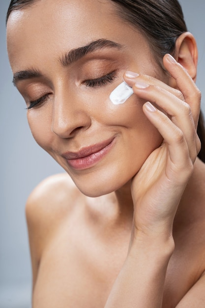 Pretty girl taking care of facial skin against grey background