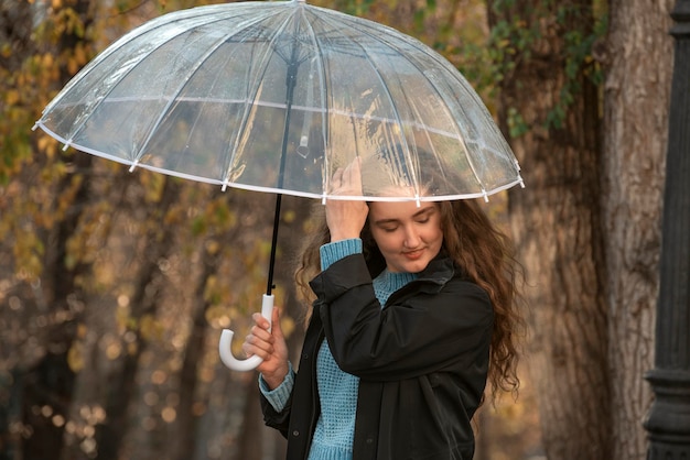 Pretty girl thoughtfully adjusts her lush hair standing under umbrella Photo of woman in autumn park