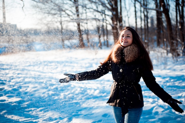 Pretty girl throws snow in a winter park