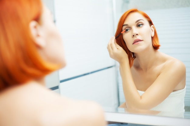 Pretty girl use care product in a bright bathroom.