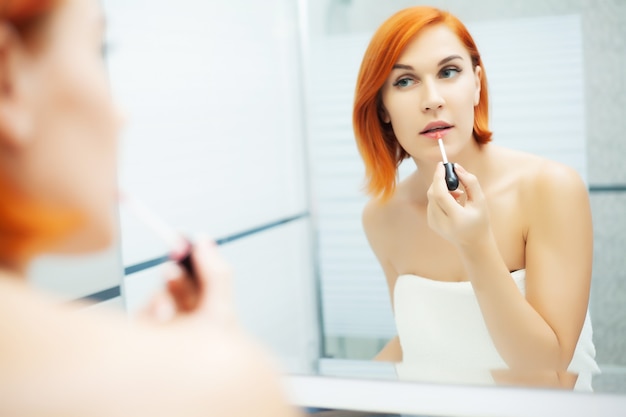 Pretty girl use care product in a bright bathroom.