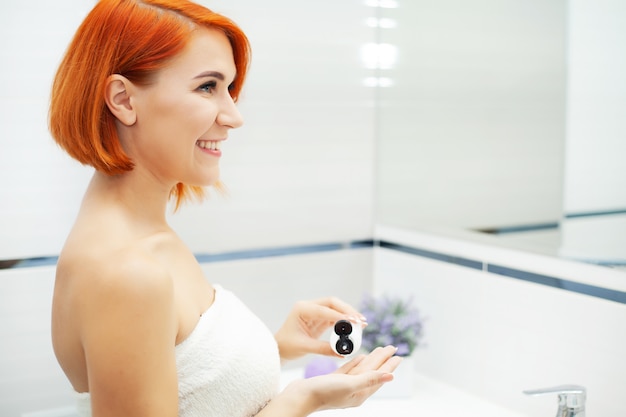 Красивая девушка использовать продукт ухода в светлой ванной комнате.