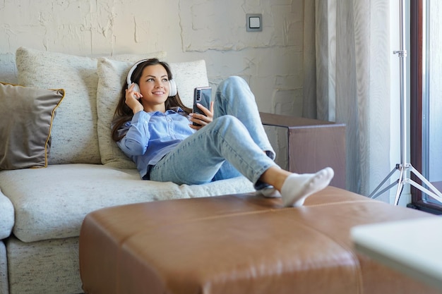 Pretty girl using her smartphone on couch at home in the living room Listening music relaxation after a hard week