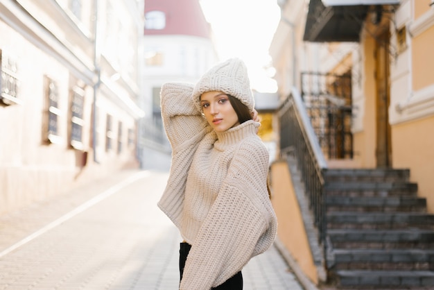 Una bella ragazza con un caldo maglione e un cappello cammina per la città d'autunno