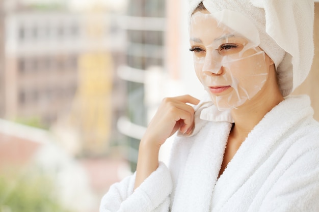 Bella ragazza che indossa la maschera per la cura del viso a casa.