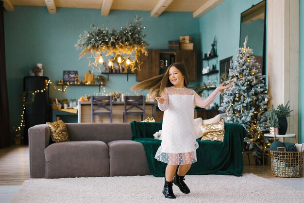 Pretty girl in a white tulle dress and black shoes is spinning in a stylish living room