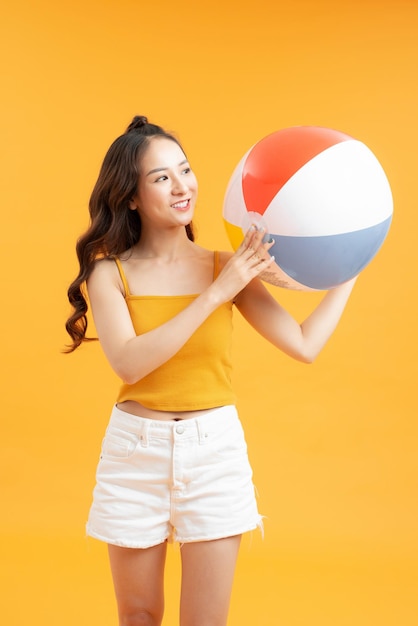 Bella ragazza con pallone da spiaggia isolato su sfondo giallo