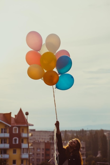 Pretty girl with big colorful balloons walking on the hills near the town. Focus on balloons