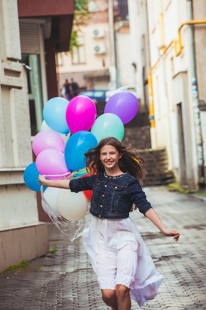 Pretty girl with big colorful balloons walking in old town