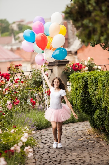 Красивая девушка с большими красочными латексными шарами позирует на улице старого города