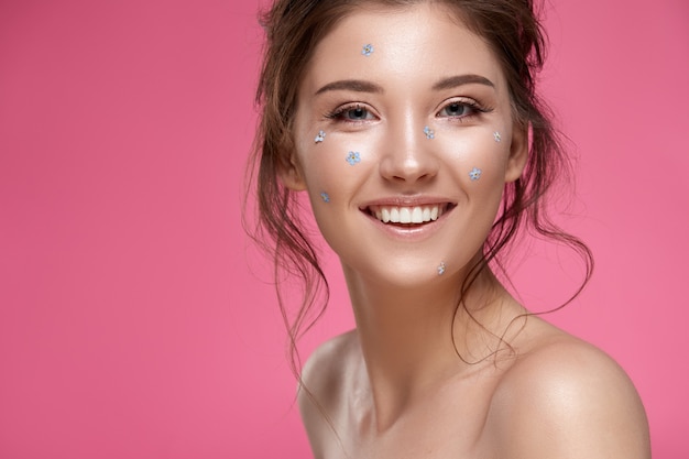 Foto bella ragazza con i nontiscordardime sul viso sorridente alla telecamera isolata sul rosa