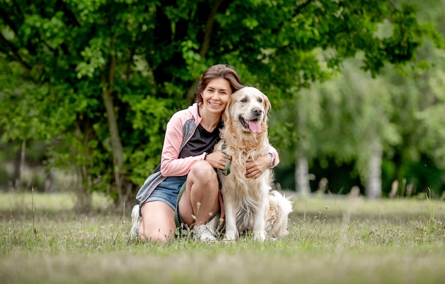 自然に座っているゴールデンレトリバー犬を持つかわいい女の子夏の公園で純血種のペット犬ラブラドールを抱き締める美しい若い女性