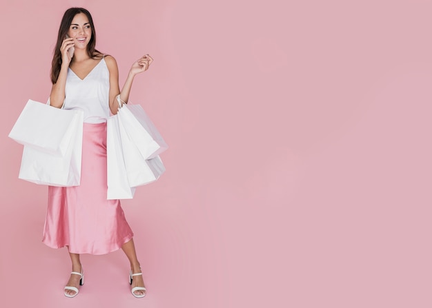 Pretty girl with many shopping bags on pink background