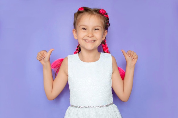 A pretty girl with pink hair shows a positive hand sign on a purple background A smiling and happy child with a thumbs up A sign of success a gesture of approval or sympathy