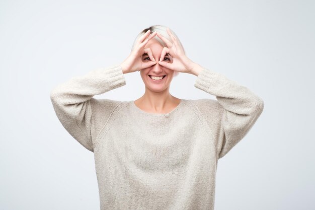 Pretty girl with surprised face holding fingers near eyes like glasses mask like super hero or owl