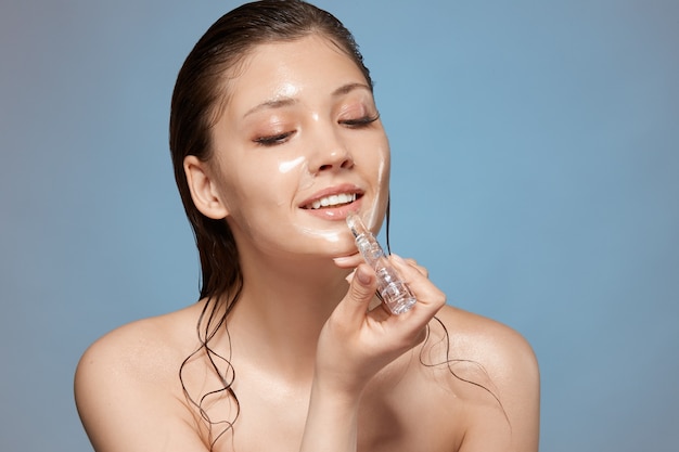 Pretty girl with wet hair and nude make-up applying lipstick with smile on her face