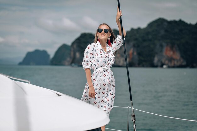 pretty girl with white dress and long curly blonde hair sitting on yacht at summertime