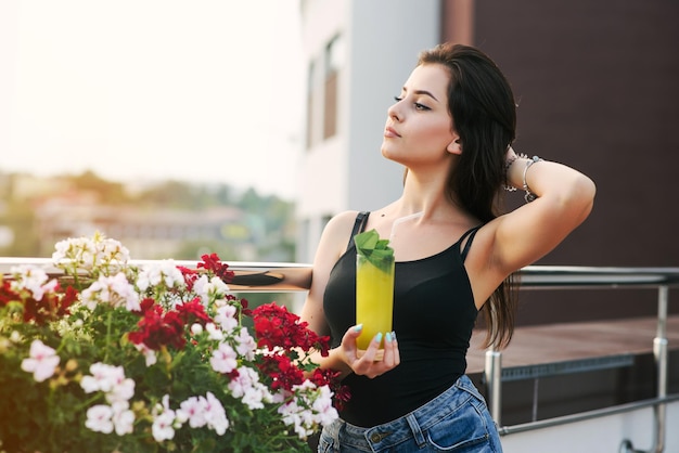 Красивая девушка с желтым коктейлем отдыхает на балконе с прекрасным видом