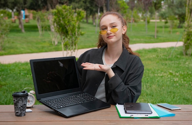 Pretty girl working at laptop in park showing screen smiling