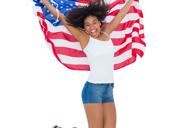 Pretty girl wrapped in american flag jumping and smiling at camera