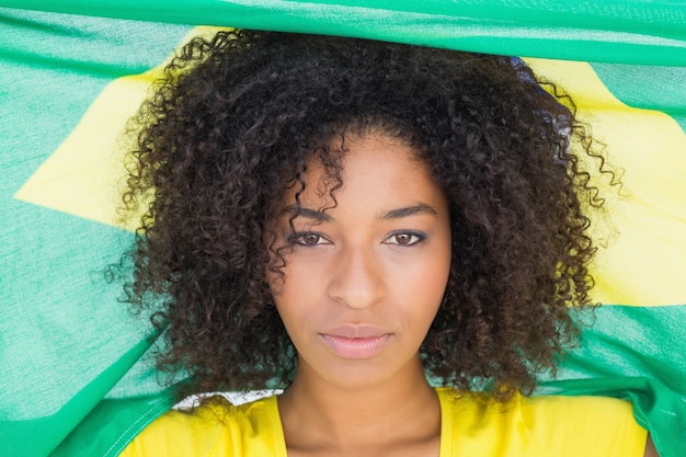 Pretty girl in yellow tshirt holding brazilian flag looking at camera