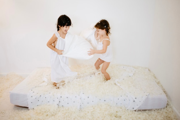 Photo pretty girls having pillows fight on mattress